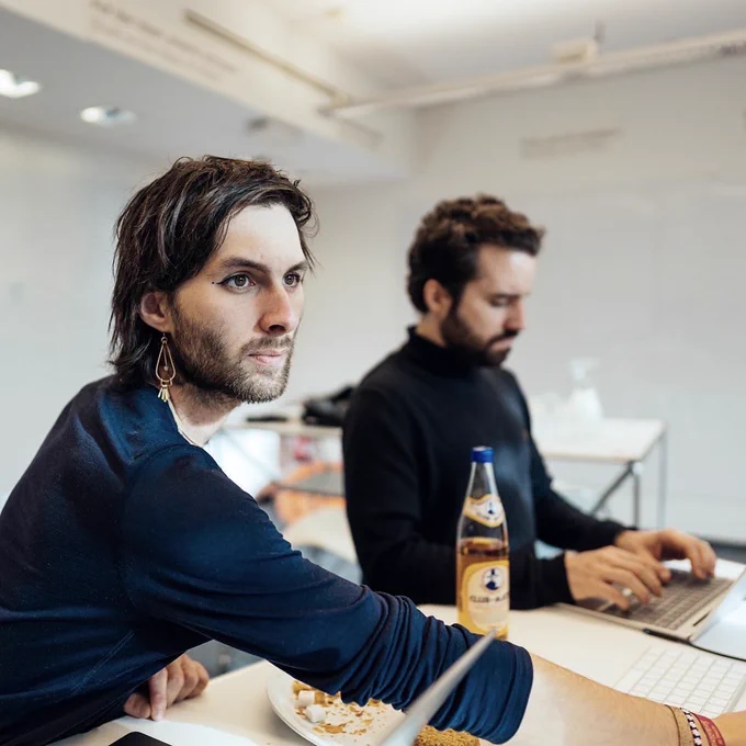 Zwei Personen sitzen an einem Arbeitstisch an Laptops