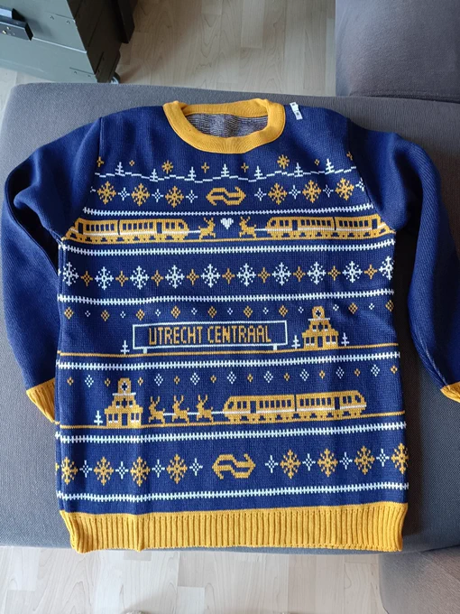Christmas jumper in blue, yellow and white showing trains being pulled by reindeer, the Dutch Railways logo, the words 'Utrecht Centraal' and general Christmas decorations