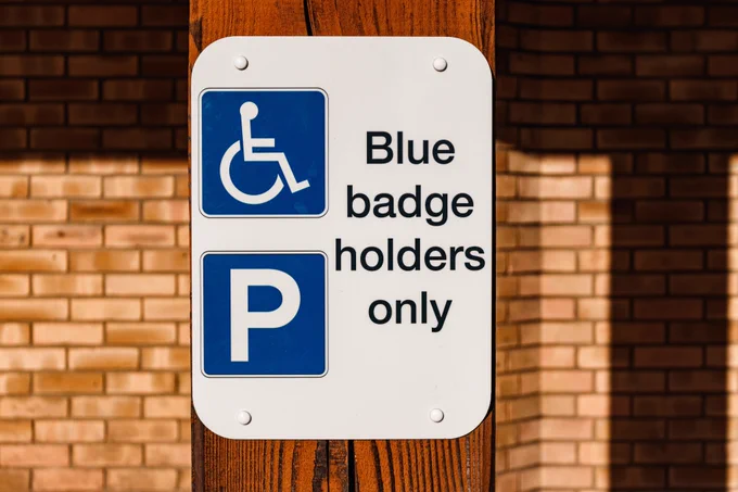 A sign on a wooden beam with the text "Blue Badge holders only" next to a wheelchair symbol and "P" parking symbol