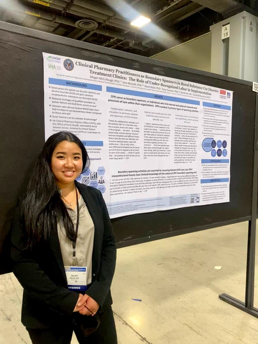 Photo of Ms. Rai standing in front of the poster