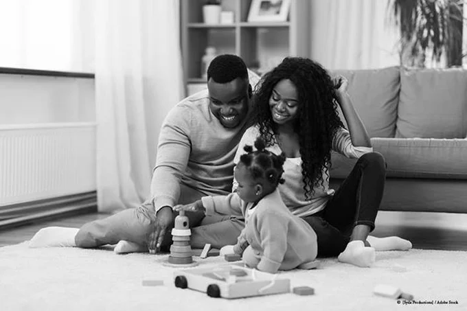 black and white photo of Black parents and toddler playing with toys on the floor