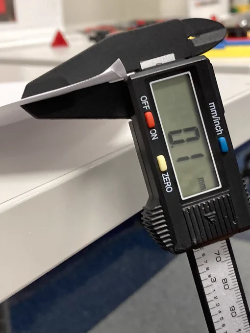 A digital caliper is clamped onto two pieces of paper