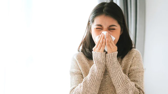 A woman sneezing into a tissue.