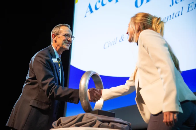 John Kobza, head of the Department of Industrial and Systems Engineering, shakes hands with graduating senior Julia Boylen through an oversized ring symbolizing the Order of the Engineer.
