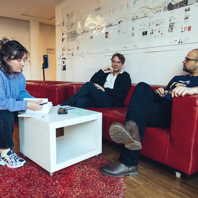 Drei Personen auf zwei Sofas mit Notizzetteln auf einem kleinen Tischchen