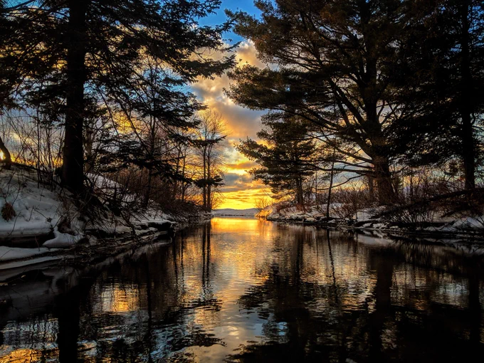 Orange sunset reflects off of a river surrounded by trees.