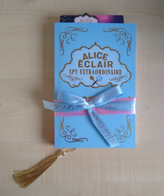 Proof of Alice Éclair Spy Extraordinaire: A Spoonful of Spying by Sarah Todd Taylor, wrapped with a blue and pink ribbon, with a gold tassel bookmark and press release inside 