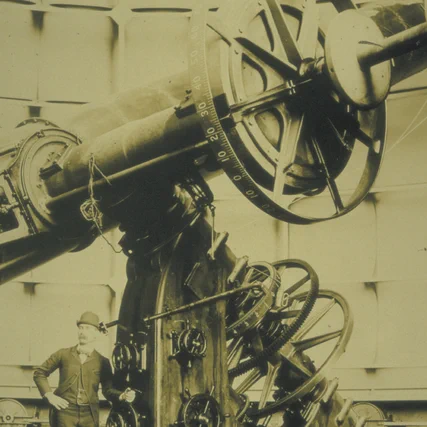 Photograph of a man standing by a large telescope, circa 1880.