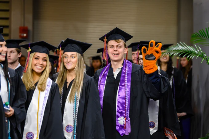 Student mascot walking up to graduate and waving at the camera.