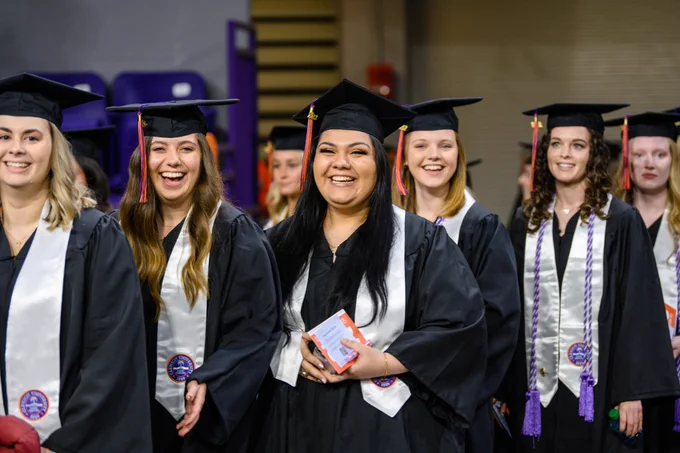 Students smiling walking to their seat at graduation.