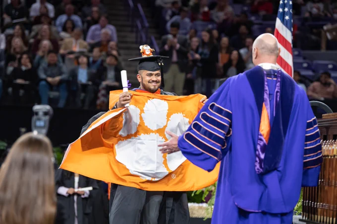 Graduate with a Clemson flag going to embrace President Clements on the stage.