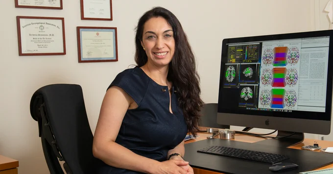 Kristina Simonyan, MD, PhD, DrMed, sits at a computer with images of brain scans displayed on the screen. 