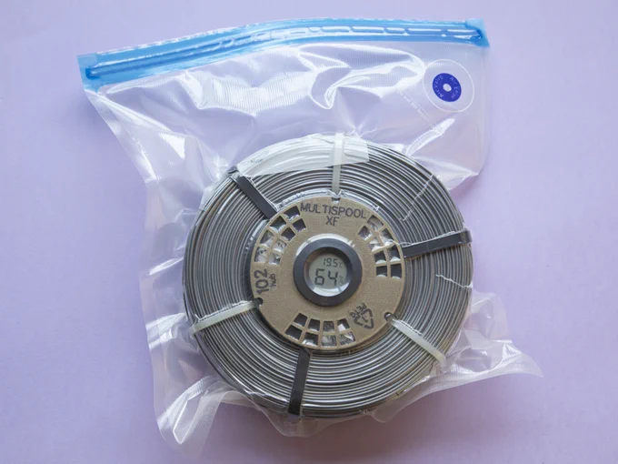 A coil inside a vacuum bag. The coil has a hub in it, and the hub is closed with a round hygrometer cap. Besides the three zipties used for securing the coil (white ties), there are three other, black zipties fixing the coil to the hub. Each ziptie is spaced approximately 60 degrees of the next; white and black zipties alternate.
