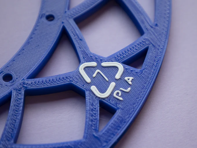 Close-up of a white PLA recycling symbol, code 7, over a blue plate with a design of squares polarly distorted.