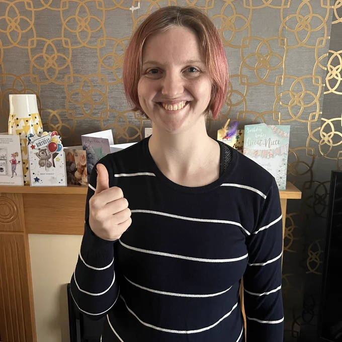 Charlie is stood in front of the fireplace, smiling with her thumb up