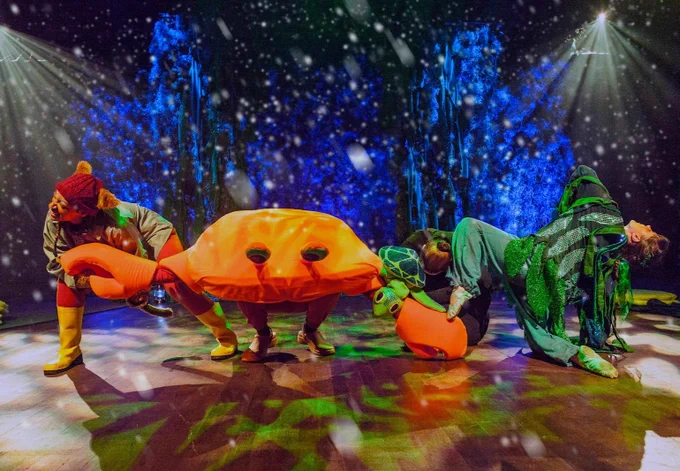 
 Standing as a group in an underwater scene, on stage, (from Left to right),  Kitty the Lighthouse Cat (brunette woman dressed with cat ears and a cold/wet weather clothing) leaning towards the left and looking. 
Carlos the Crab (Large Orange soft Crab Costume) facing forwards, Tilly The Turtle (Green soft Puppet) swimming downward. On the floor in a  angular pose, facing back with left knee lifted looking upwards, the Sea Fairy (brunette woman dressed in seaweed looking costume).
Lit by beautiful blues and greens
