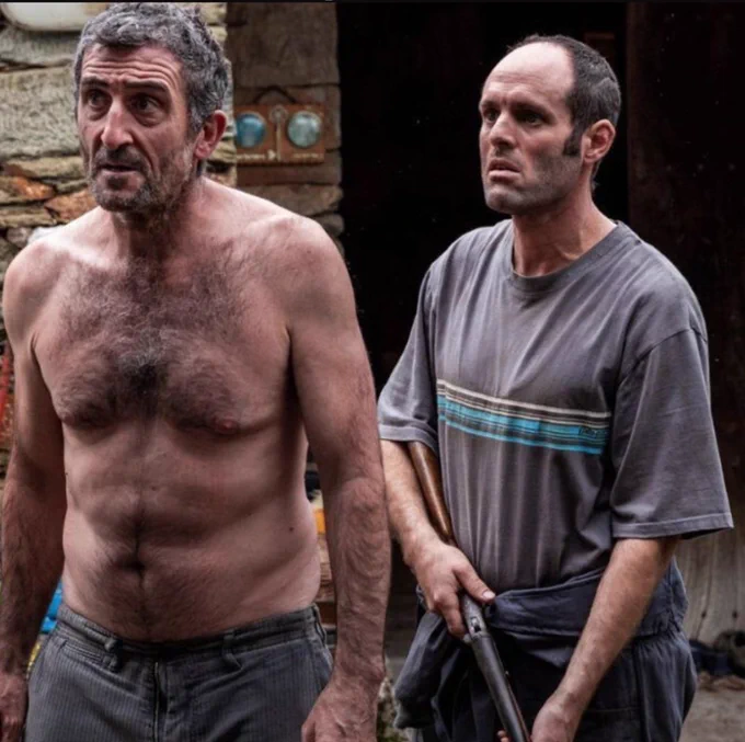 Aparecen os irmáns Anta, da película As Bestas. Un sen camisola e outro cun rifle, en posición ameazante.