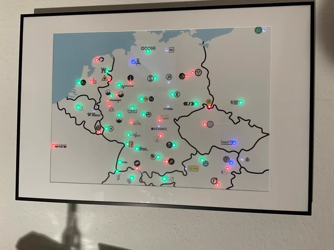 A printed and framed map on a posted. It shows a part of central europe with some logos of a random collection of hackerspaces with spaceapi. each logo is next to a controllable rgb led (in traditional case). at a white wall in the openlab augsburg