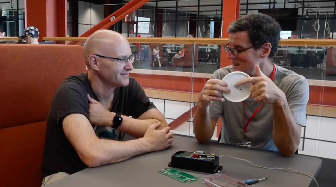 Jon and Mitch looking at an electronic project, which is sitting on a table between them.