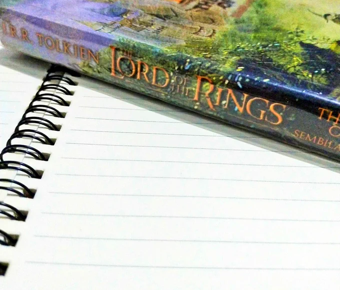 Close up of an empty page of a notebook, with a Lord of the Rings book on top of it.