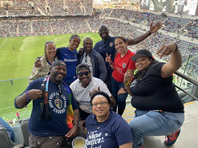 Group of nine people at a soccer stadium excited for the match to start.