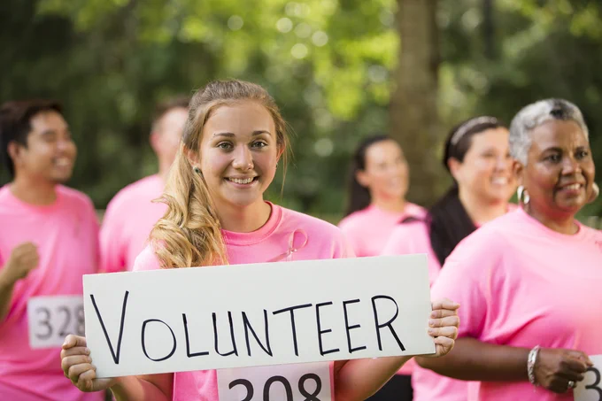 Image of a group of volunteers dressed in pink, with the person at the front holding up a sign that says 'volunteer'
