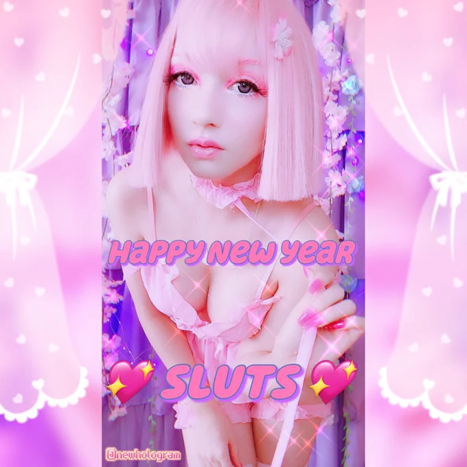 New is a fair-skinned mixed race enby with a bubblegum pink bob wig leaning forward in front of a purple curtain backdrop decorated with fairy lights and cherry blossoms. They're done up in fluffy eyelashes and bright pink makeup. They wear a soft pink lingerie set and pink nails. The photo is adorned with sparkles and drawn-on heart curtains. The text reads: HAPPY NEW YEAR 💖SLUTS💖