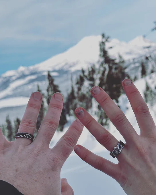 His and her hands showing engagement rings against a snowy mountain background