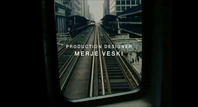 A still from the opening title sequence of The Bear Season 1 Episode 7 showing aboveground subway tracks as seen through the door of a subway car. The credit for PRODUCTION DESIGNER: MERJE VESKI is in sans serif white text on top.