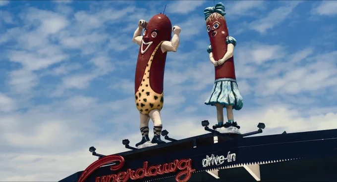 A still from the opening title sequence of The Bear Season 1 Episode 7 showing the roof of Chicago landmark Superdawg drive-in which has two large statues of anthropomorphized hot dogs standing on top of it