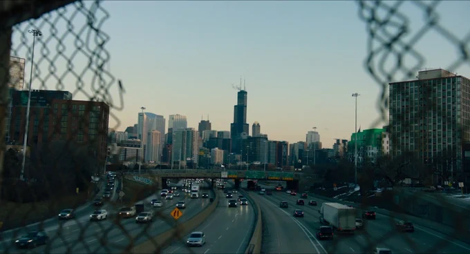 A still from the opening title sequence of The Bear Season 1 Episode 7 showing the Chicago skyline over a highway as seen through a chainlink fence