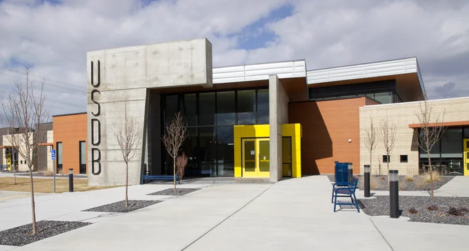 a picture of the modern school with high glass walls by the entry and a bright yellow door.