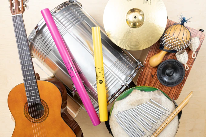 An image showing a selection of musical instruments in a music studio. A variety of drums, shakers symbols and a guitar. 