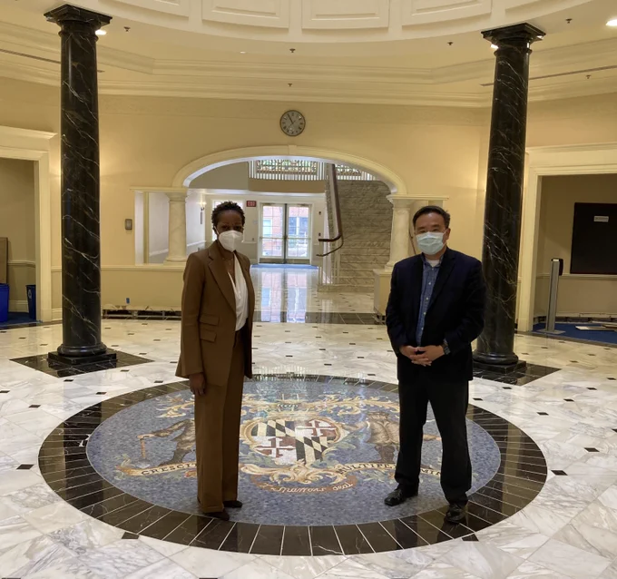 A man and a woman both wearing face masks stand a few feet apart from one another in the Maryland House of Delegates. 