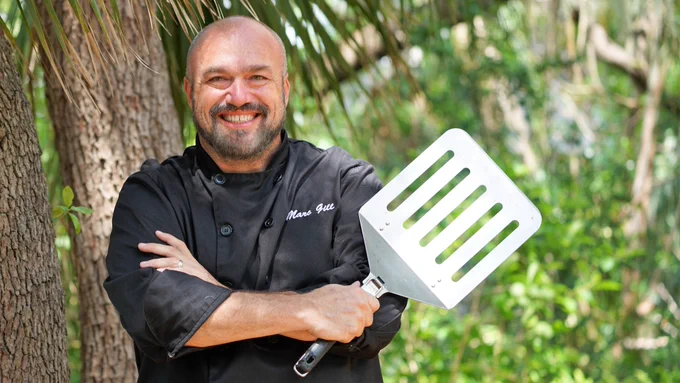 A chef standing under a tree holding a large spatula