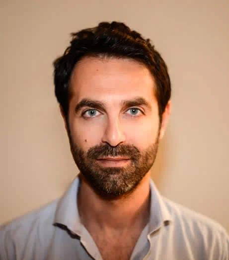 Photo of Shaun. He is a man with a Mediterranean complexion, dark hair and beard. He is wearing a light blue shirt and smiling.