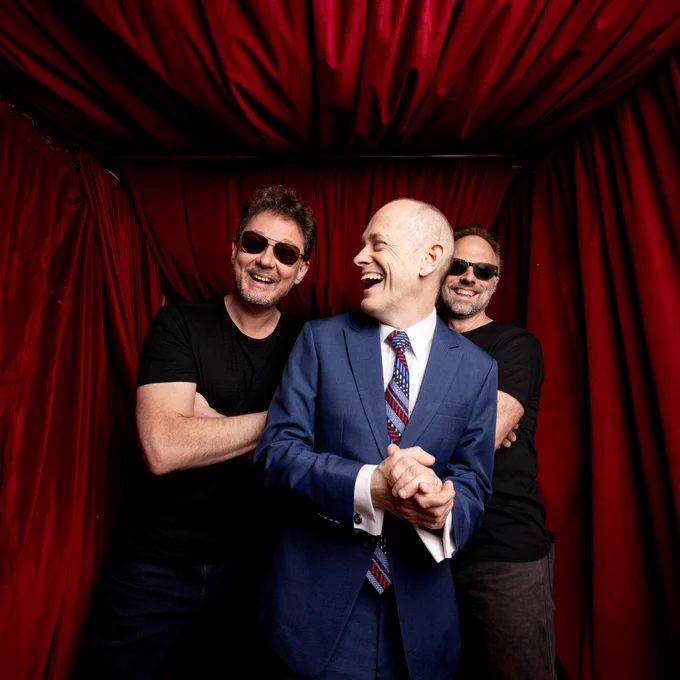Tripod laughing in front of a red drape. 