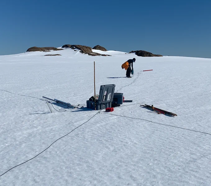 Magnetotelluric (MT) station being installed in snow, showing instrument casing and magnetometers prior to burial.  Rock outcrop in background.