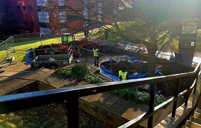Looking down on workers digging a hole by the path outside the Edward Boyle Library