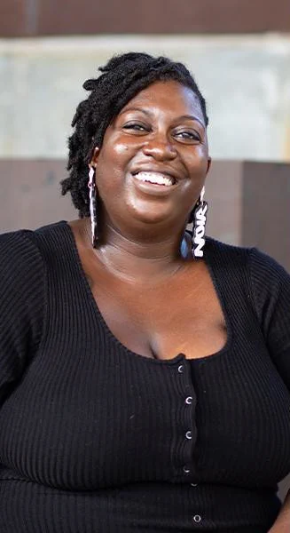 Dr. Tatiana Benjamin, a young Black woman, smiling. She's wearing a black shirt and large earrings that say "NOIR"