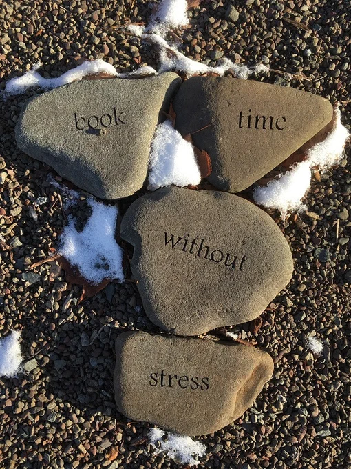 Word garden rocks that say "book time without stress" surrounded by some snow