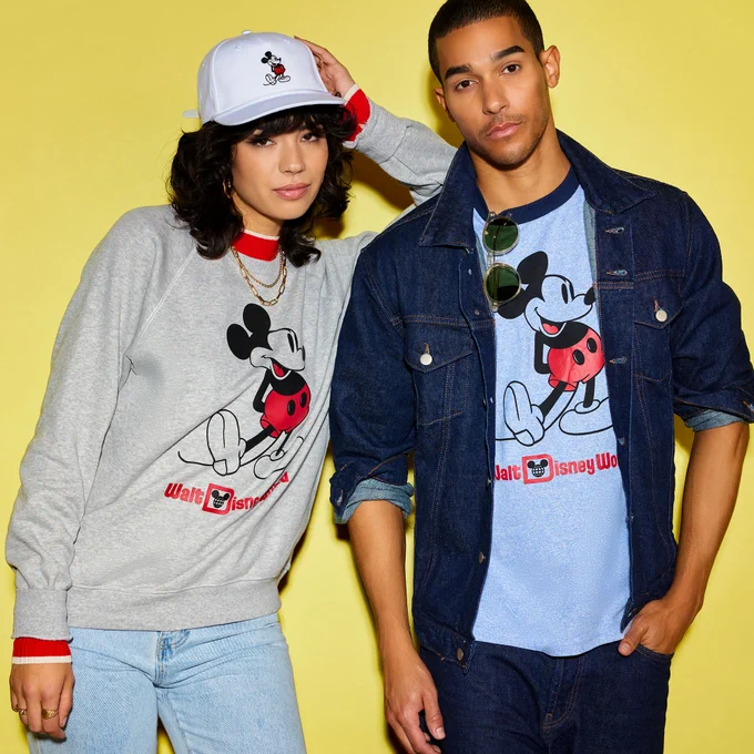 Woman wearing Classic Mickey gray sweatshirt with Classic Mickey white baseball cap. Man is wearing jacket with  a Classic blue Mickey t-shirt. 