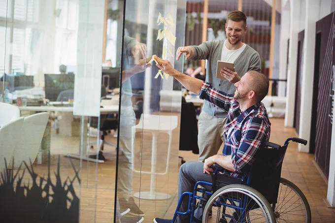 Person seated in a wheelchair working on a development design board with a coworker.