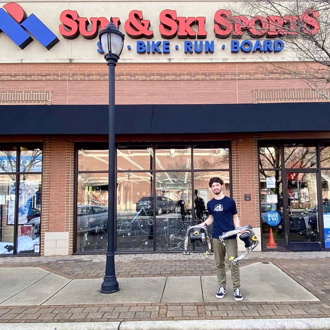 The storefront in the background with a young employee holding up 2 donated bike trainers