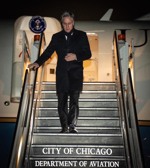 Secretary Blinken walks down the stairs of a plane. The Department of State logo is on the plane door behind him. The words "City of Chicago. Department of Aviation" are printed on the stairs. 