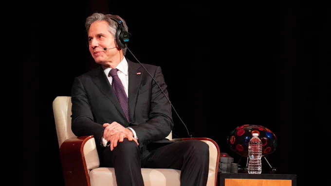 Secretary Blinken is sitting, looking to his right, and smiling.