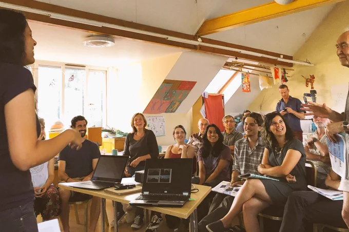 The Bristol Cable holds a meeting at Windmill Hill City Farm. People are sat in a bright room at desks, they look engaged and are smiling.