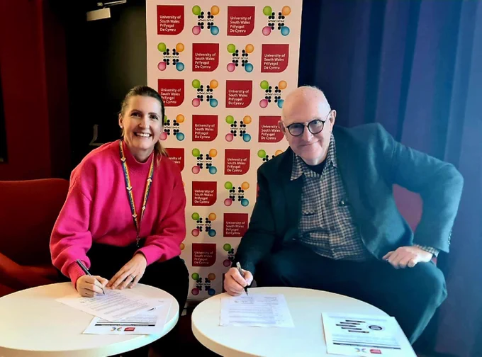 Two people sat at a table holding pens, ready to sign documents
