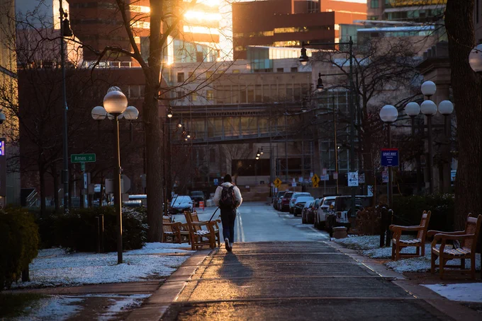 Person with backpack walking towards Ames Street on MIT campus.