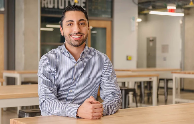 Nick Kaviani smiles as he sits at a table in a workshop. 